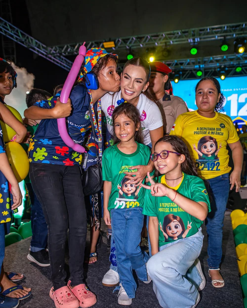 Débora Menezes abraçando crianças apoiadoras no palco