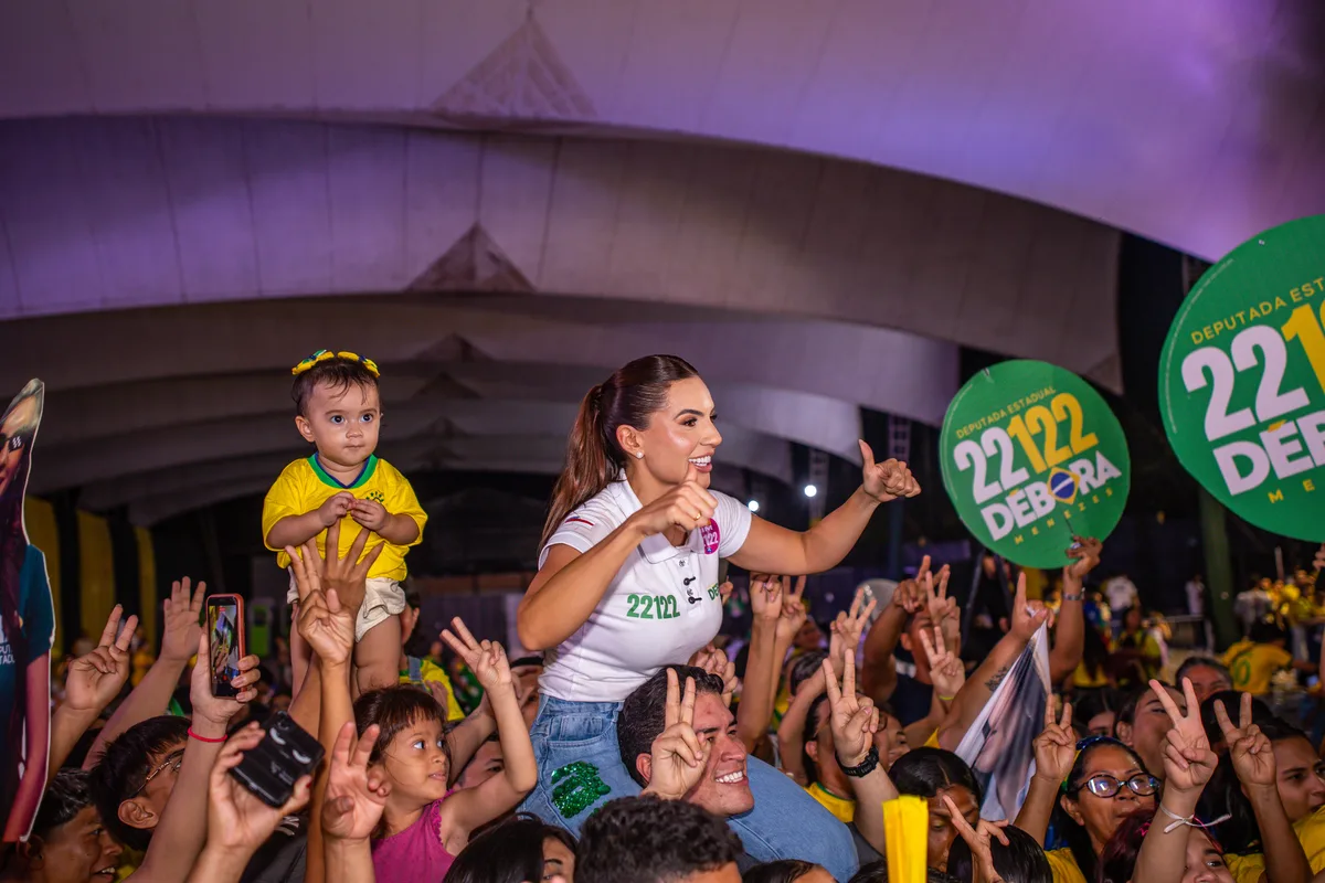 Débora Menezes com criança no colo, cercada de apoiadores